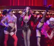 Cher performing Welcome to Burlesque in a black velvet jacket and corset with backup dancers on a stage