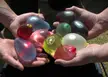 Close-up of friends with fair skin holding a selection of colorful, water-filled balloons outdoors.