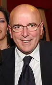 Mario Oliverio, a bald man with glasses in a pinstripe suit, smiling next to a woman with hoop earrings.