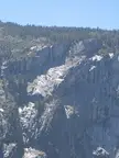 A tall waterfall cascading down a rocky cliff with evergreen trees under a blue sky in a California landscape.