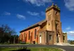 A brick church with a tall bell tower in Bathurst, New South Wales, surrounded by trees and benches.