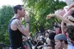 Tattooed man in a black tank top singing into a microphone for a crowd at Tompkins Square Park