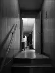 Black and white vintage photo of a person in white robes standing in a hallway viewed through a doorway