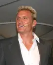 Lundgren smiling in a grey suit jacket and white shirt with a headset microphone