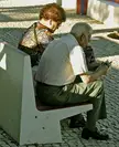 Elderly couple sitting on a white concrete bench, woman in leopard print reading a magazine