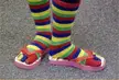 A woman wearing colorful striped toe socks and pink flip-flops standing on a grey carpet.