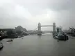 London Tower Bridge over a river with a naval ship and boats under a cloudy sky