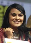 Camila Mendes smiling behind a microphone wearing a red floral print dress