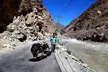 A man in a blue t-shirt and brown pants with a loaded scooter on a road in a mountainous river valley near Dah village