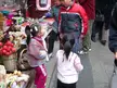 Petite Asian girls in Qi Bao and streetwear gathered around a colorful craft stall at an outdoor street market.