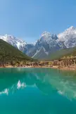 Jade Dragon Snow Mountain with a turquoise lake reflecting snow-capped mountains and green hills