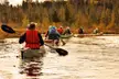 A group of eight people in canoes with paddles paddling through a river with autumn foliage in the Adirondacks
