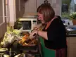 Plus-size woman with brown hair and glasses in a green apron basting a roasted turkey in a kitchen