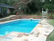 Custom stone swimming pool with a slide and stone patio in a backyard with a person in a blue shirt