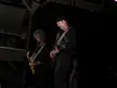 Foghat performing on a dark stage with electric guitars, wearing black shirts and a baseball cap
