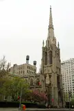 Grace Church, a tall Gothic-style church with a high spire, next to city buildings with a person walking a dog