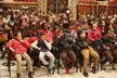 Pregó de Santa Eulàlia: a group of people in hoodies, cardigans, and leopard print seated in a wooden hall