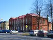 Kelmė street scene with a red brick building, parked cars, and bare trees under a blue sky