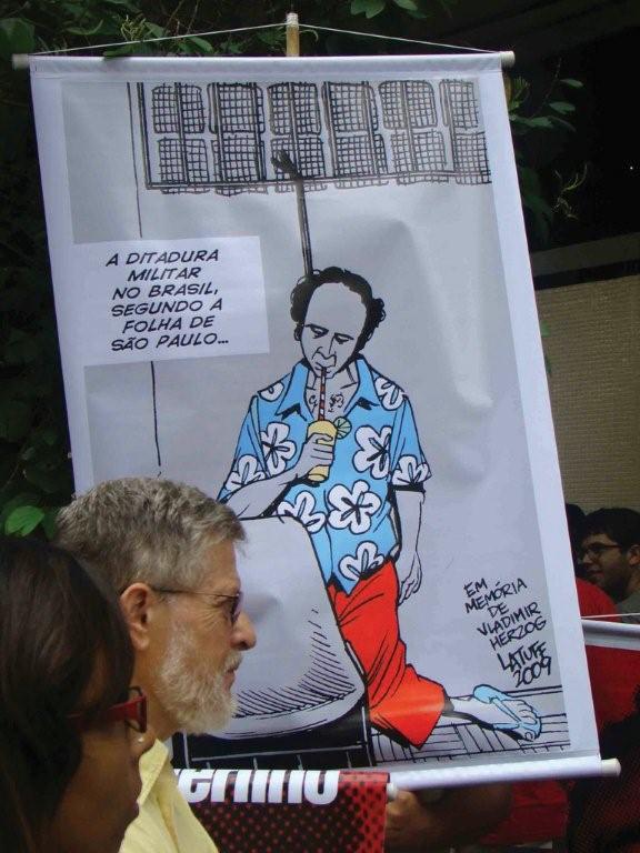 2009 event in Brazil. A poster from political cartoonist Carlos Latuff with the sarcastic legend: The military dictatorship in Brazil, according to the newspaper Folha de São Paulo. It is based on the infamous photo of Herzog by the Brazilian intelligence and repression agency Departamento de Operaç