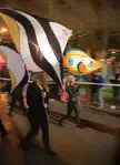 Two blonde women in black leather jackets walking at the Parramatta Luminary Parade with funny fish-shaped umbrellas