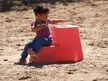 Amelia wearing a purple t-shirt and blue denim skinny jeans sitting on a red play structure in the sand