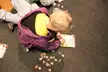 A blond child in a purple hoodie and yellow shirt lying on a carpet putting together a jigsaw puzzle