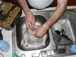 A person in a white shirt stuffing a raw turkey over a double kitchen sink