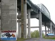 Mercier Bridge in Kahnawake with concrete pillars, graffiti reading KAHNAWAKE IRONWORKERS, and a blue-roofed building.