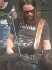 Ponderosa performing on an outdoor stage, featuring a man with long hair and sunglasses playing a black bass guitar.