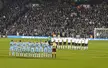 Soccer players in light blue, white, and maroon athletic wear standing in lineups on a green field before a crowd.
