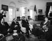 Zulfiqar Ali Bhutto and John F. Kennedy with other men in dark suits and ties in a formal living room