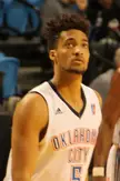 Tokoto wearing a white Oklahoma City basketball jersey with blue and orange trim in an indoor sports arena.