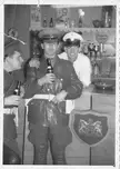 British Army soldiers in uniform jackets and hats smiling with bottles at a bar counter