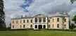 Mõdriku manor, a large two-story yellow house with columns on a green lawn under a cloudy sky