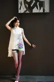 Chinese beautiful girl in a white floral print shirt, denim shorts, and purple tights posing by an abstract oil painting