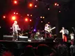 Six musicians playing instruments on a concert stage with red lighting and a PILSEN LOVE backdrop.