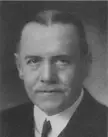 Fredrik Ramel in a black and white close-up portrait wearing a dark suit, white shirt, and tie.
