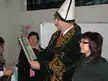 A man in a white miter and green velvet robe with gold embroidery holding a book, standing with two women.