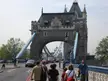 People in casual streetwear and a black BMW car on a road leading to Tower Bridge in London
