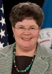 Caryn Wagner smiling in a grey textured blazer and turquoise bead necklace