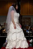 A beautiful plus-size woman with fair skin in a white strapless satin wedding dress and veil on a red carpet