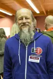 John Gilmore smiling in a blue zip-up hoodie and name tag, close-up in a group setting.
