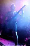 Annotations of an Autopsy member with spiky hair playing a bass guitar in a dark tank top on a concert stage