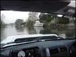 View from a car interior looking through the windshield at a white boat docked on a riverbank with trees.