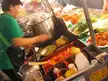 Petite Korean girl with fair skin in a green t-shirt and apron preparing street food at a market stall