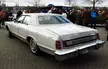 White Ford LTD vintage luxury car on brick pavement with a group of people in leather jackets and blue jeans