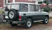 Rear view of a silver and grey Toyota Land Cruiser Prado, a JDM car, parked by a brick building.
