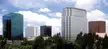 Modern office buildings and green trees in a California city skyline under a blue sky