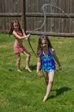 Two friends in a pink bikini and blue dress playing with a water hose in a grassy yard by a wooden fence