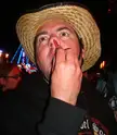 A man in a straw hat and black hoodie putting a red object in his nostril during a challenge.